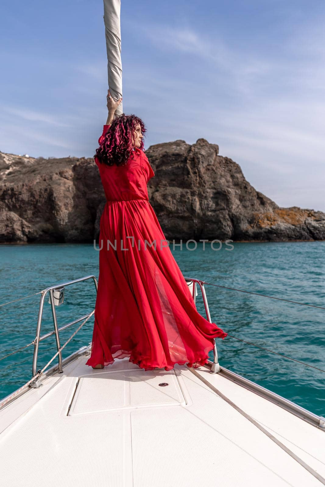 Attractive middle-aged woman in a red dress on a yacht on a summer day. Luxury summer adventure, outdoor activities