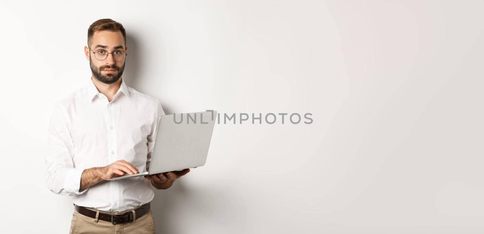 Business. Young handsome businessman working on laptop, doing job on computer, standing over white background by Benzoix