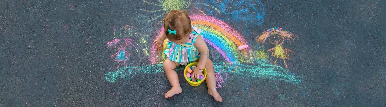 Baby draws a rainbow on the pavement with chalk. Selective focus. by yanadjana
