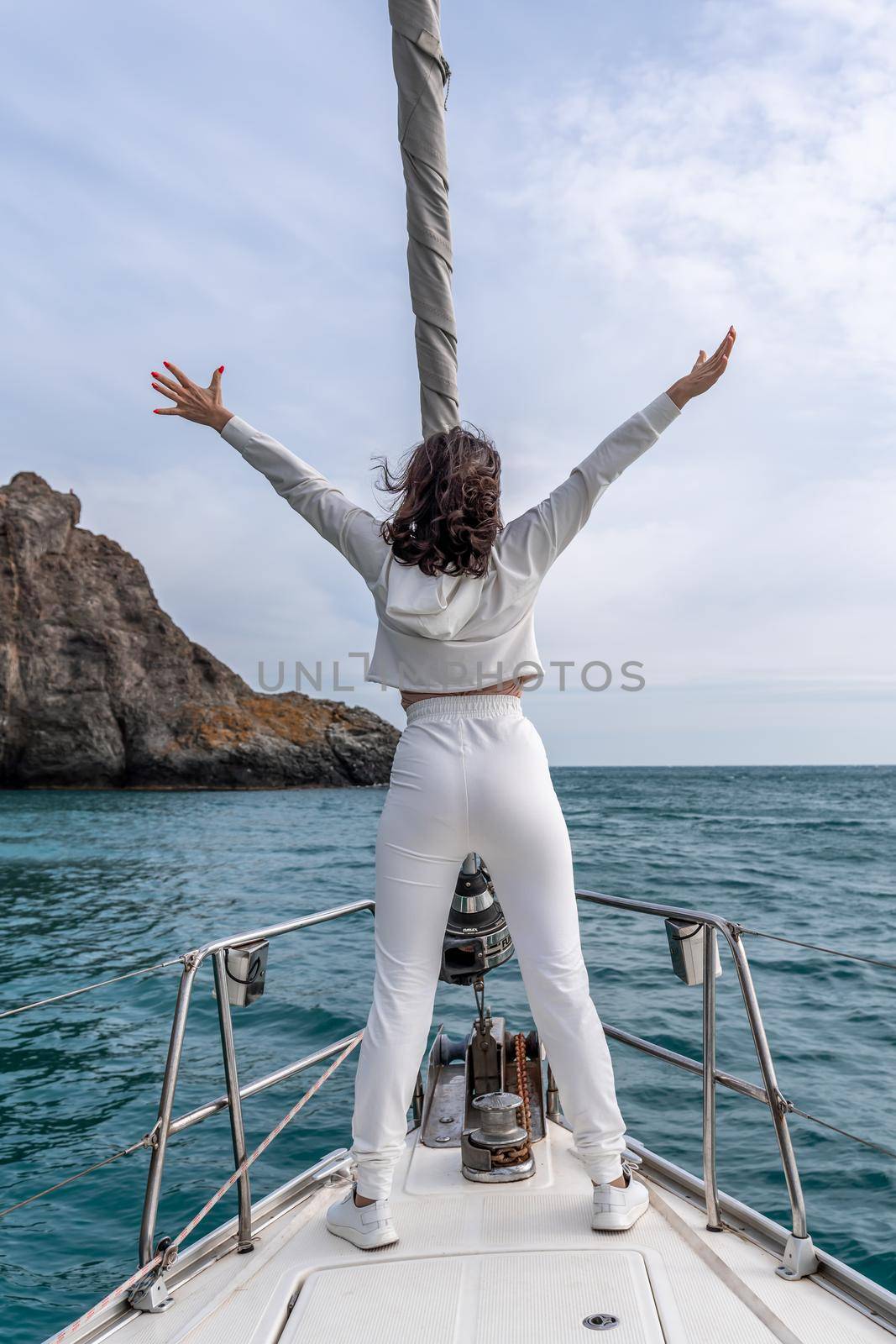 Woman standing on the nose of the yacht at a sunny summer day, breeze developing hair, beautiful sea on background.