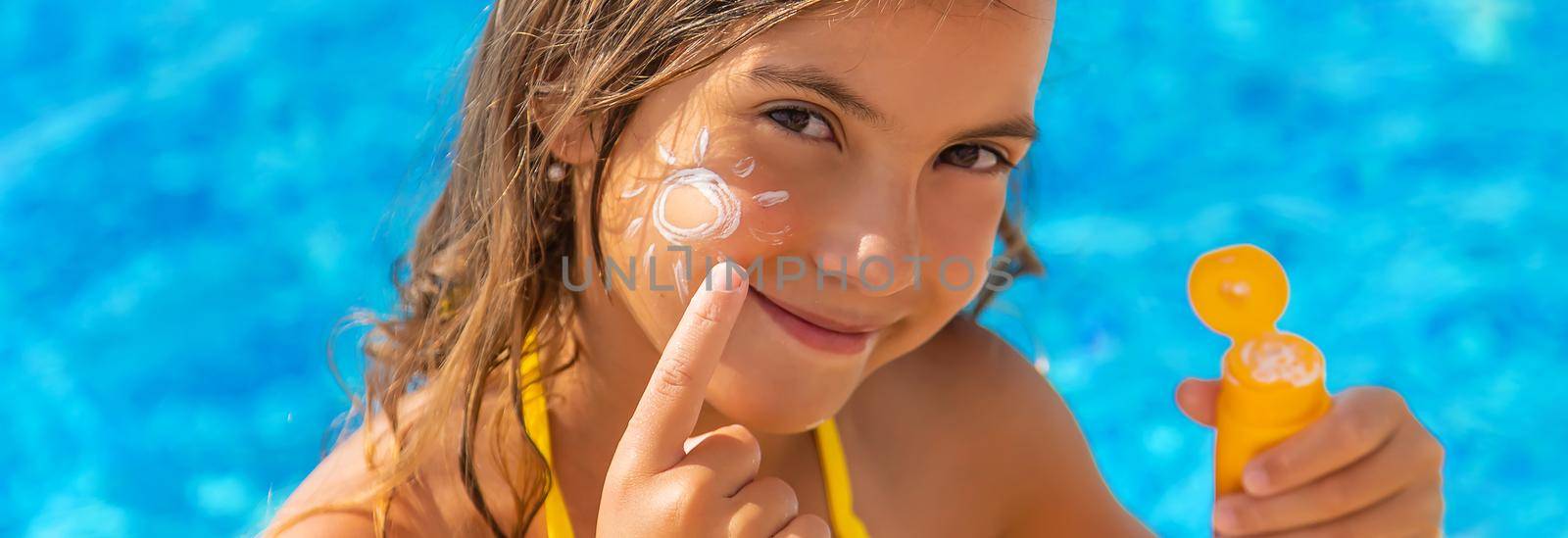 The child is putting sunscreen on her face. Selective focus. Kid.