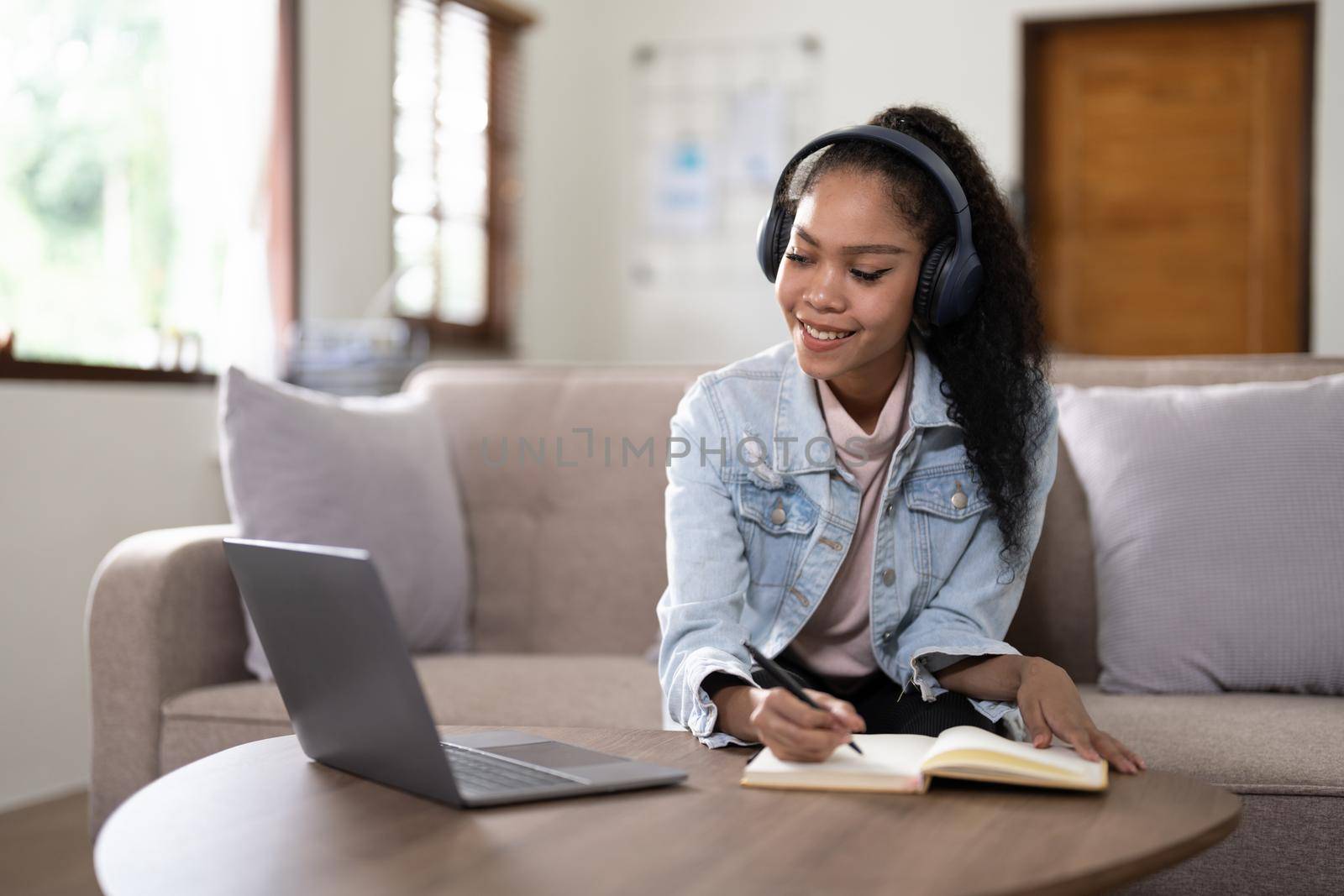 mixed race woman wearing headphones watching webinar write notes study online with online teacher, african female student learning language computer course on laptop listen translate lecture by nateemee