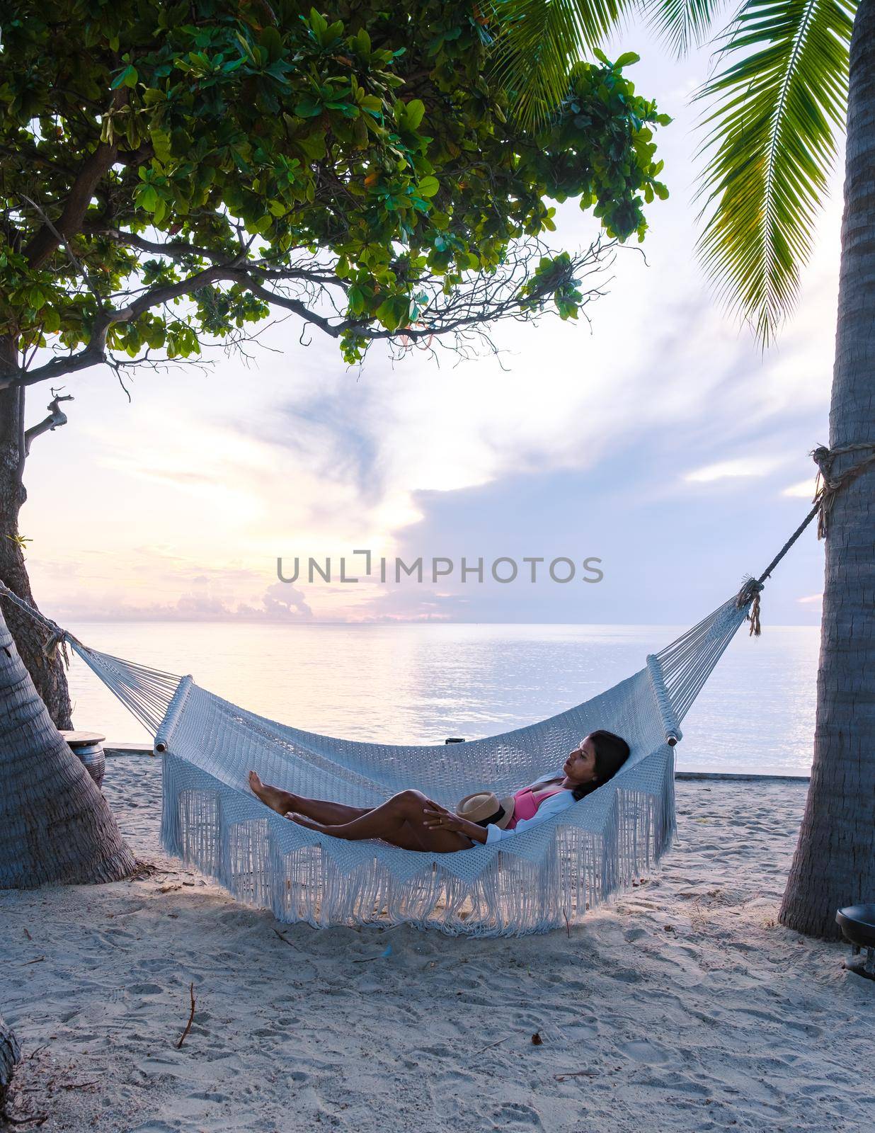 women watching sunrise in a White hammock under palm trees at a tropical beach in Thailand Hua Hin by fokkebok