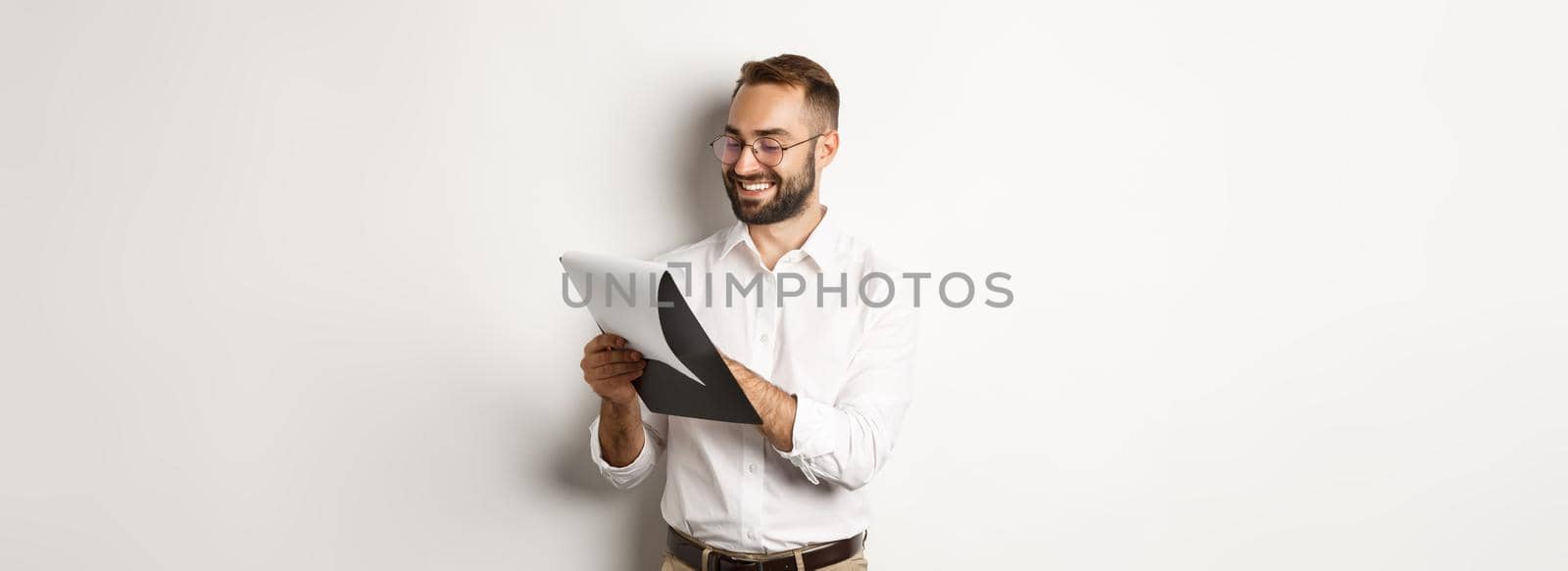 Man looking satisfied while reading documents, holding clipboard and smiling, standing over white background.