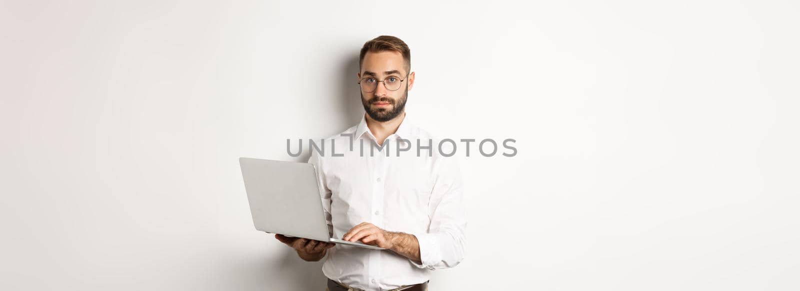 Business. Young handsome businessman working on laptop, doing job on computer, standing over white background.