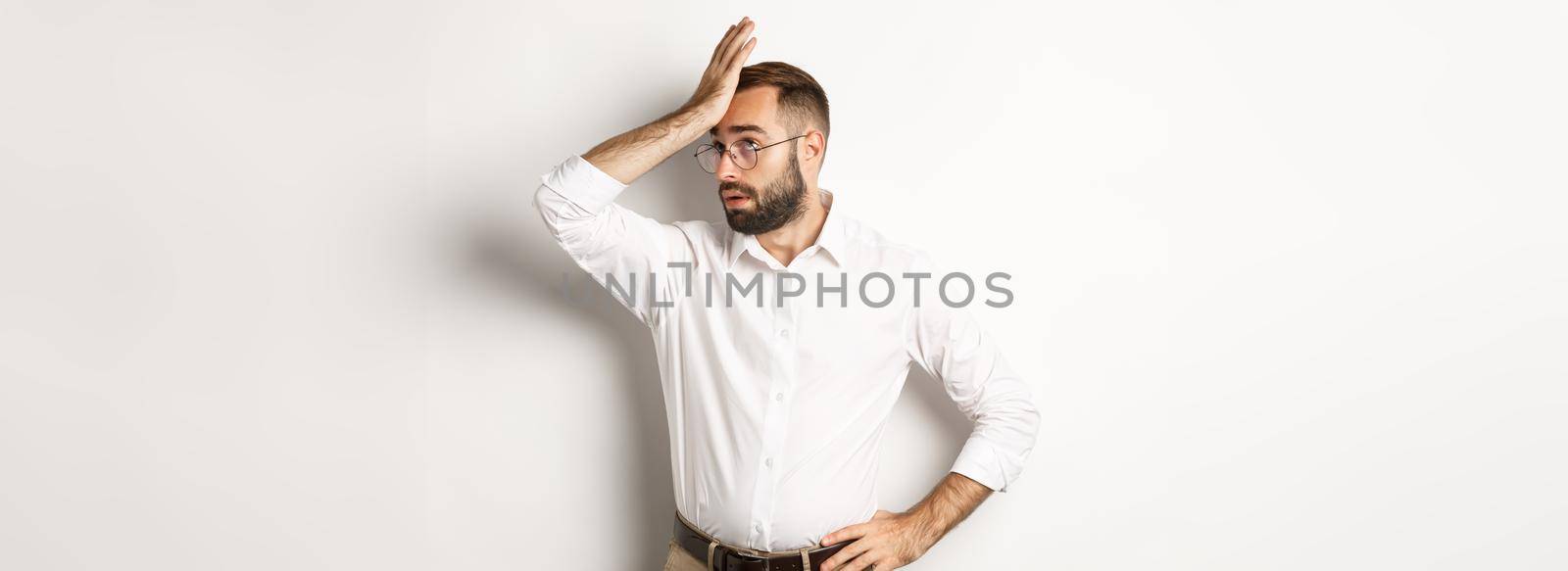 Annoyed man manager roll his eyes and slap forehead, facepalm from something tiresome, standing over white background.