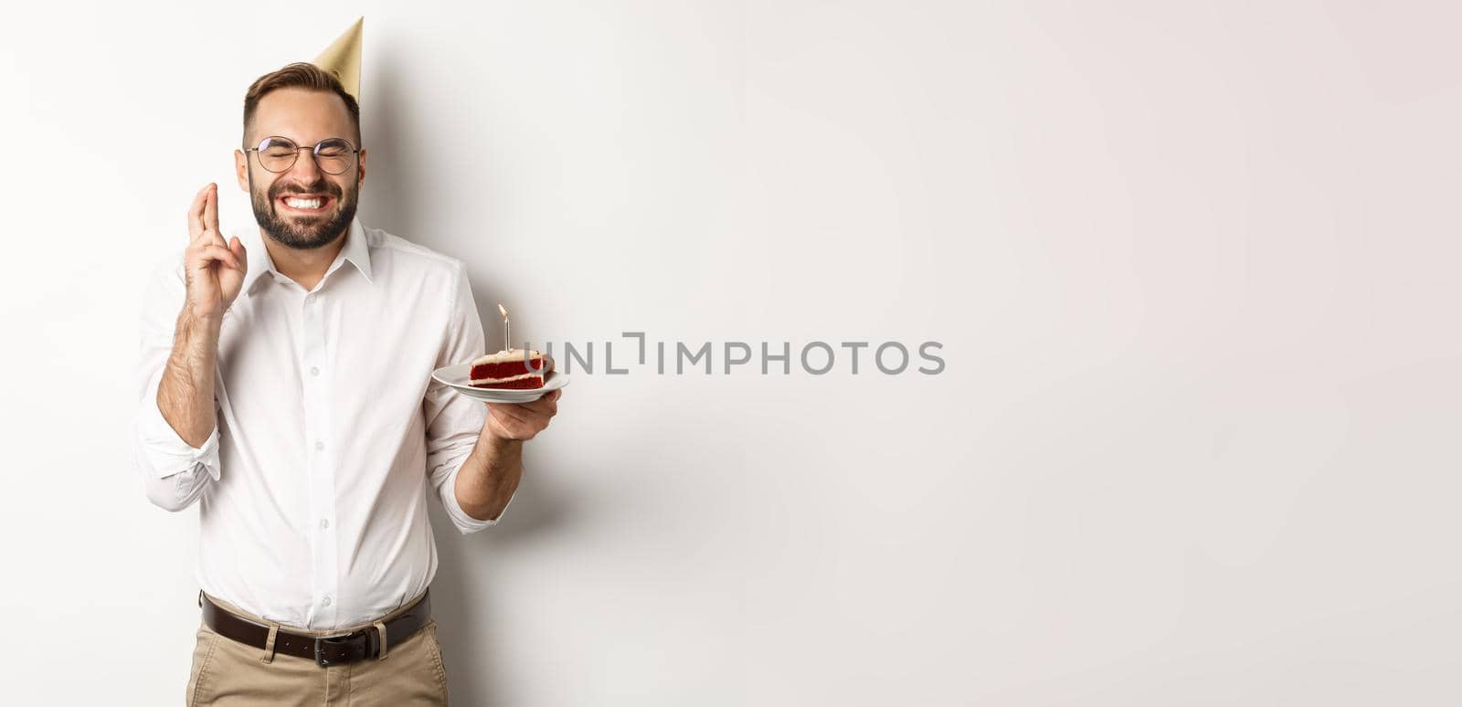 Holidays and celebration. Happy man making wish on birthday cake, cross fingers and smiling excited, having b-day party, white background by Benzoix