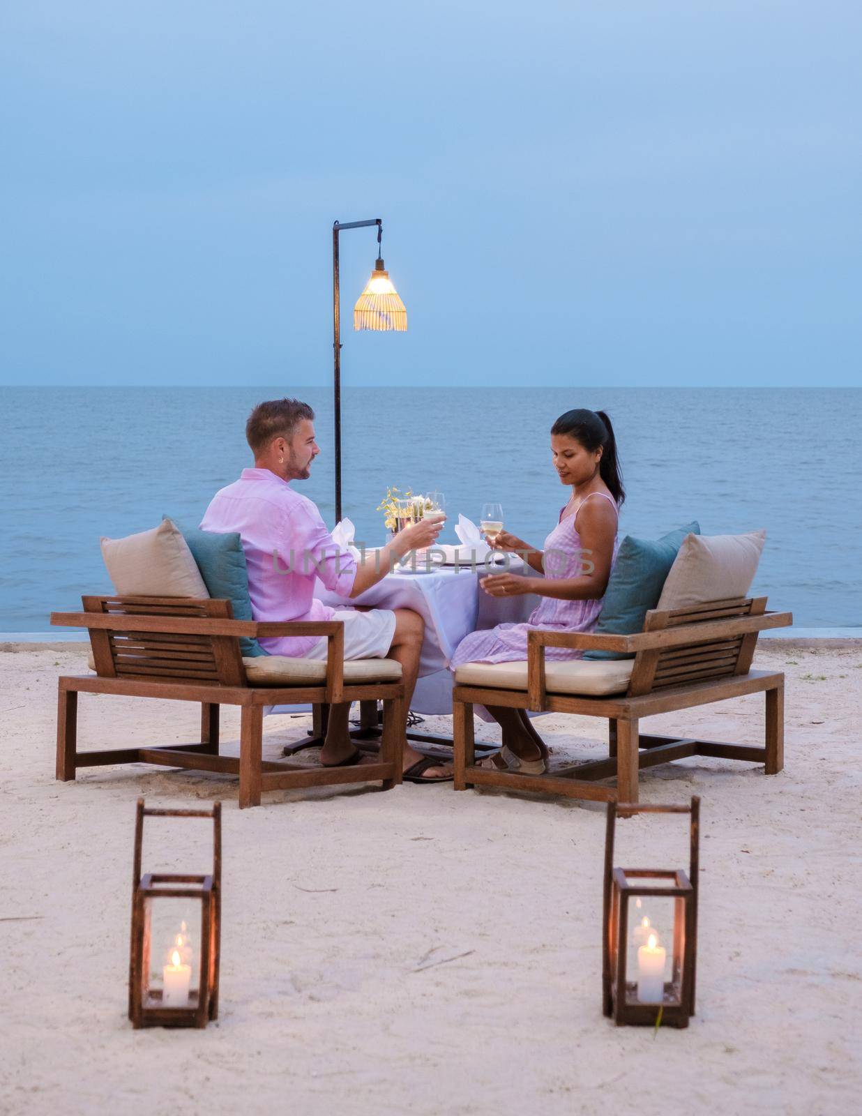 Couple men and women having a romantic dinner on the beach in the evening by fokkebok