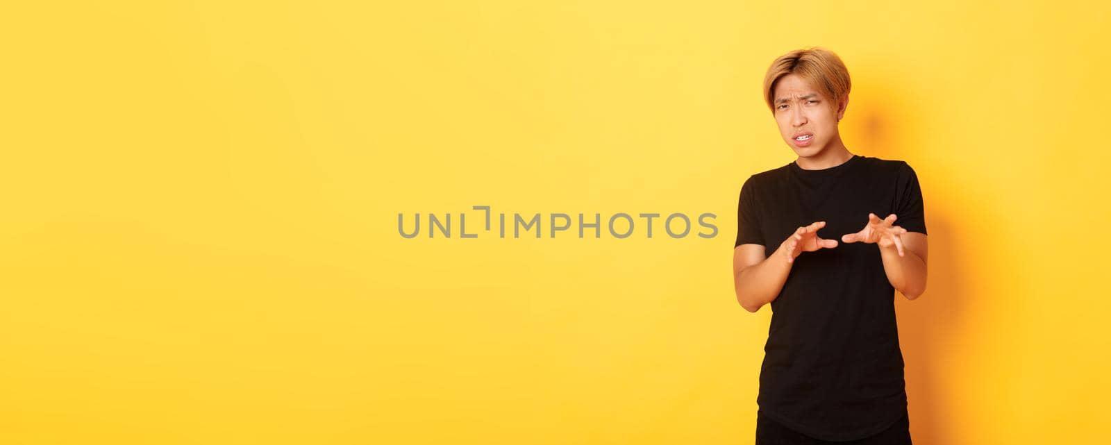 Portrait of disgusted picky asian guy, refusing and grimacing, standing yellow background.