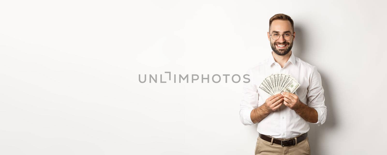 Smiling handsome man holding money, showing dollars, standing over white background. Copy space