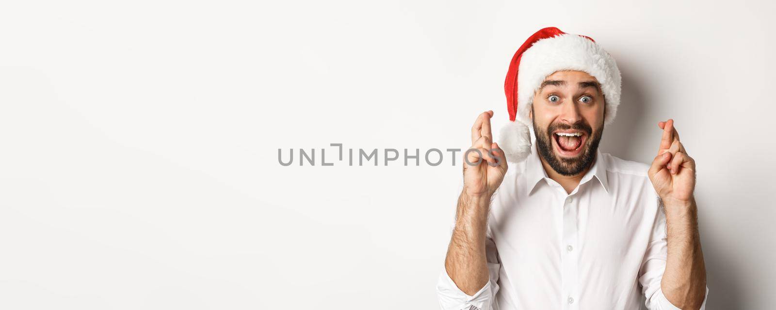 Party, winter holidays and celebration concept. Happy man in santa hat making christmas wish, cross fingers for good luck and looking excited, white background.