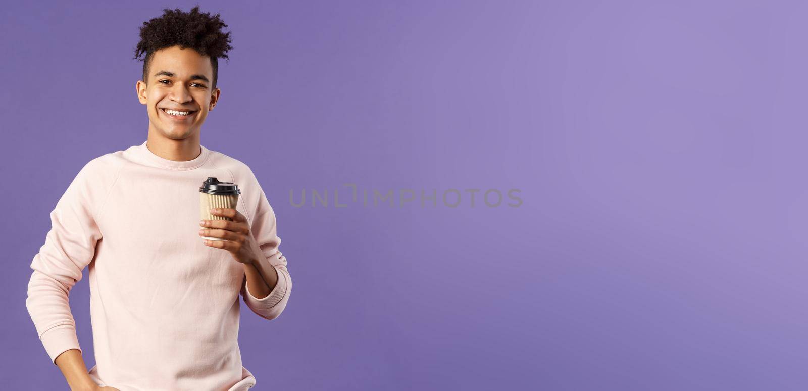 Lifestyle, cafe, eating-out concept. Portrait of cheerful young hispanic guy holding take-away cup of coffee, drinking and smiling camera, waiting for someone, thanking coworker for bringing cappucino.