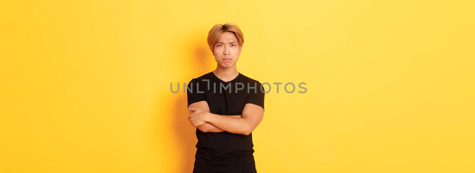 Worried serious-looking and concerned asian guy, cross arms chest and frowning at camera, yellow background by Benzoix