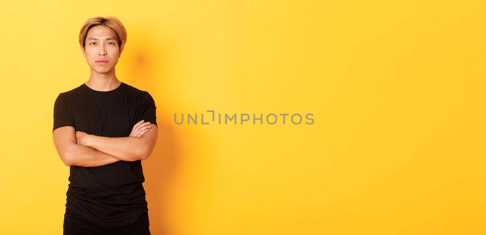 Portrait of serious-looking confident asian guy in black t-shirt, cross arms chest, standing yellow background by Benzoix