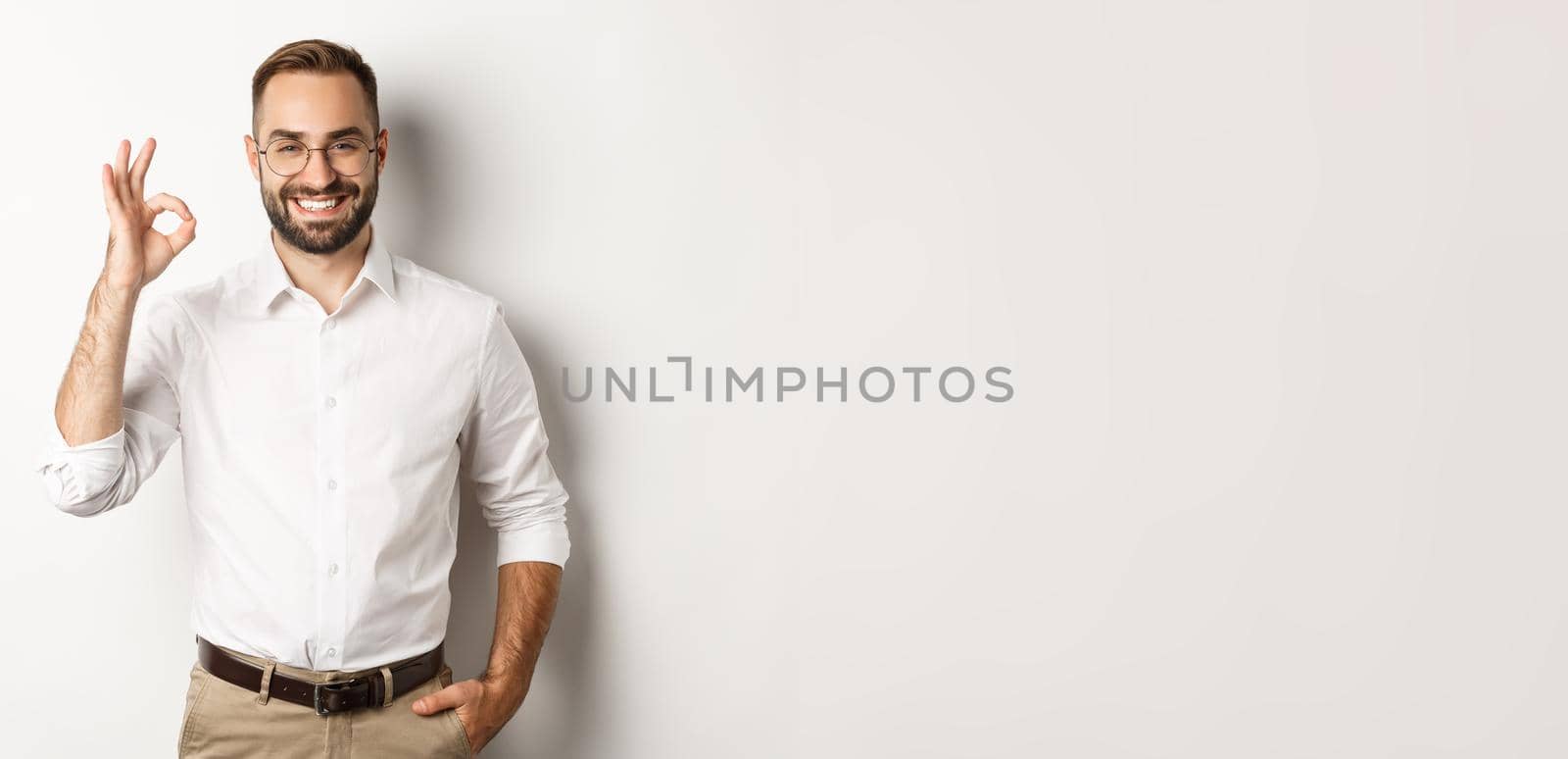 Satisfied businessman smiling and showing ok sign, approve and like something good, standing over white background.