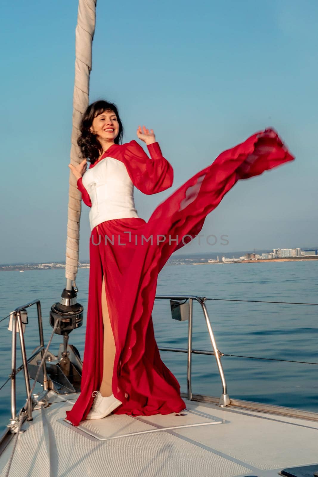 Attractive middle-aged woman in a red dress on a yacht on a summer day. Luxury summer adventure, outdoor activities. by Matiunina