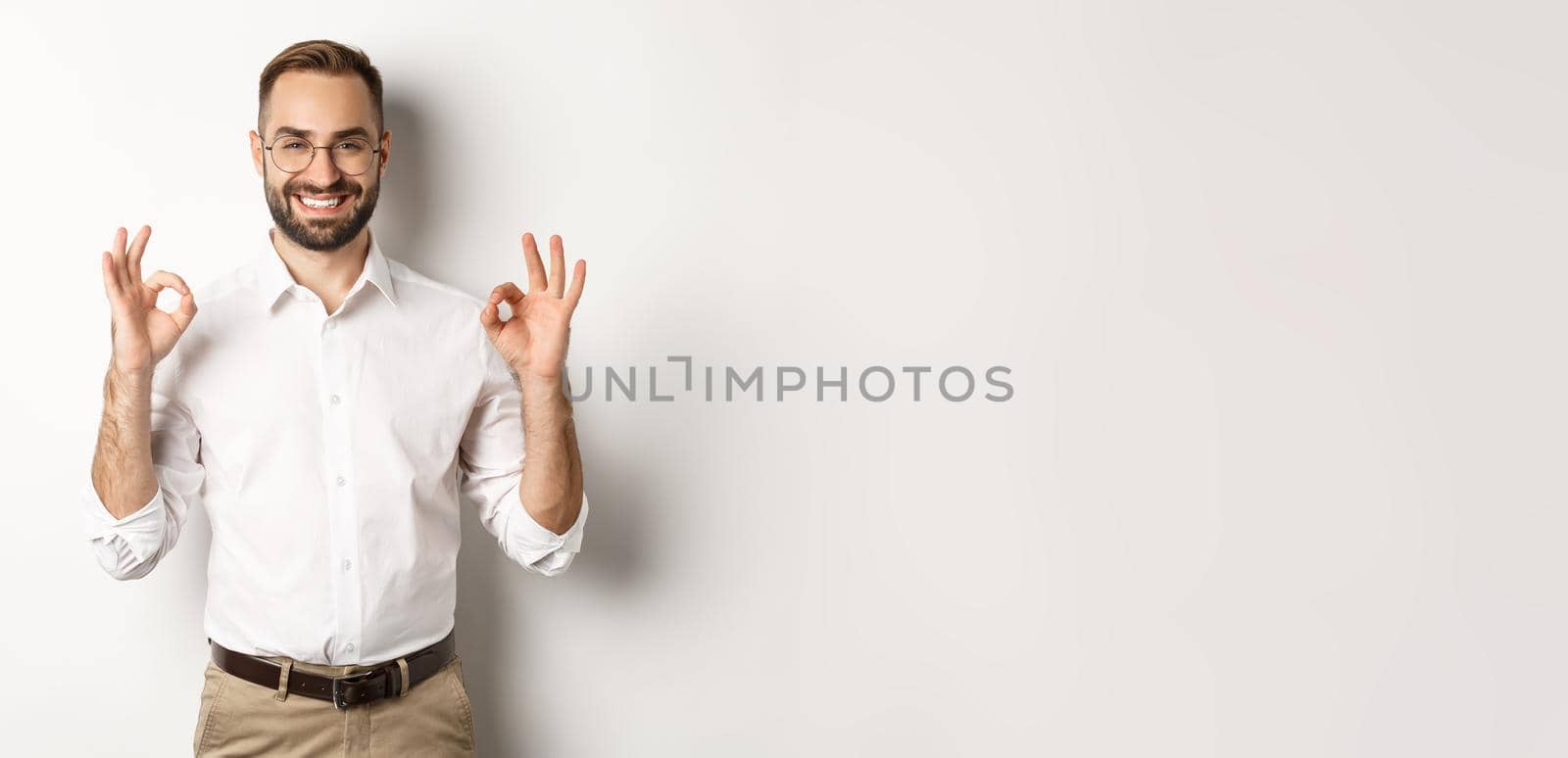 Satisfied handsome businessman showing ok sign, gurantee quallity, standing pleased against white background.