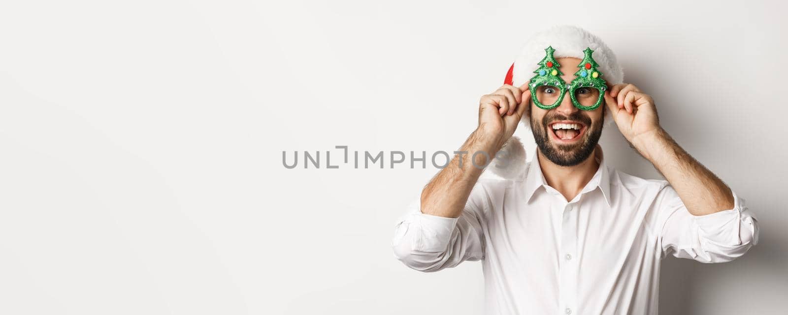 Close-up of happy man celebrating christmas holidays, wearing party glasses and santa hat, enjoying New Year, white background by Benzoix
