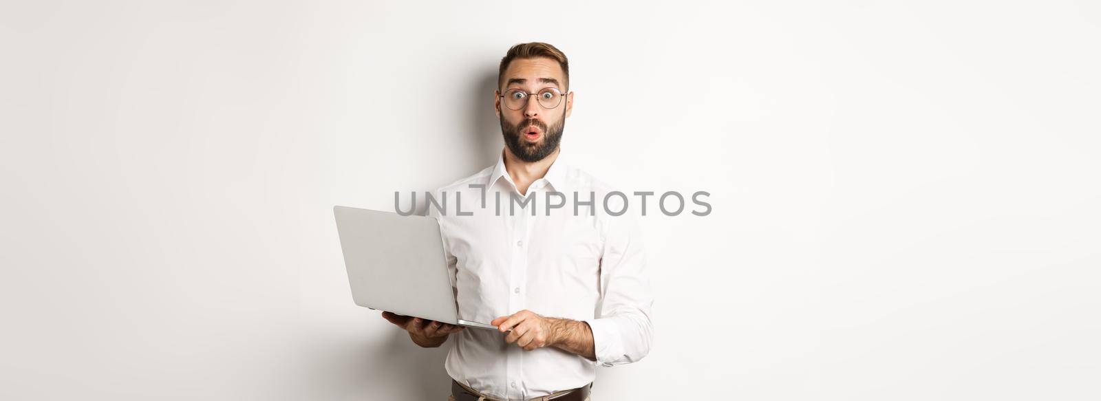 Business. Surprised business man holding laptop and looking interested, standing with computer against white background.