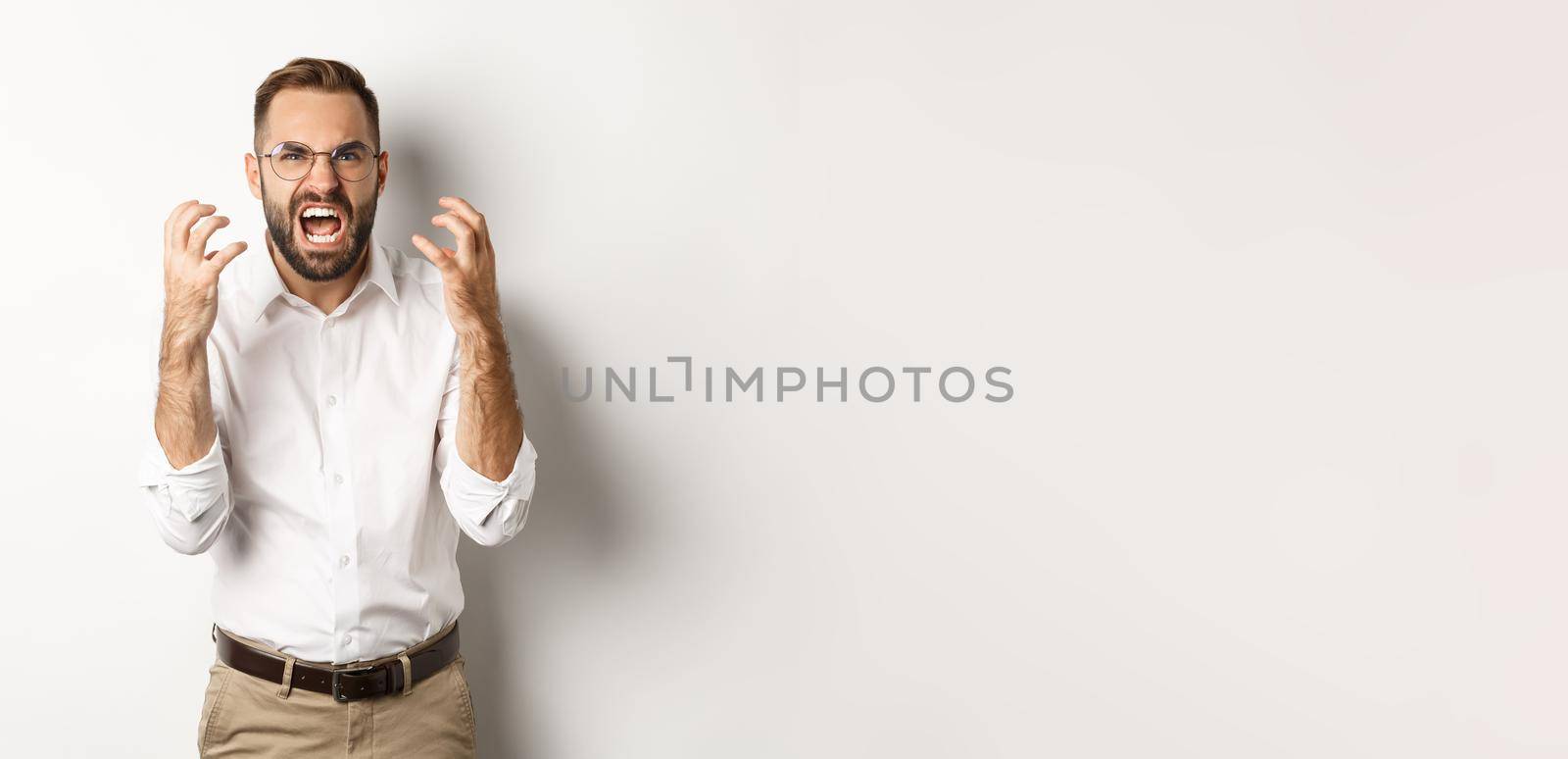 Frustrated and angry man screaming in rage, shaking hands furious, standing over white background.