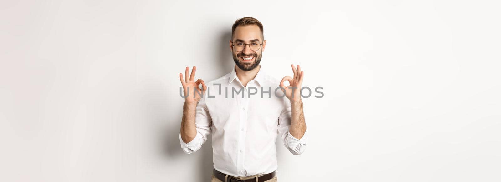 Satisfied handsome businessman showing ok sign, gurantee quallity, standing pleased against white background.