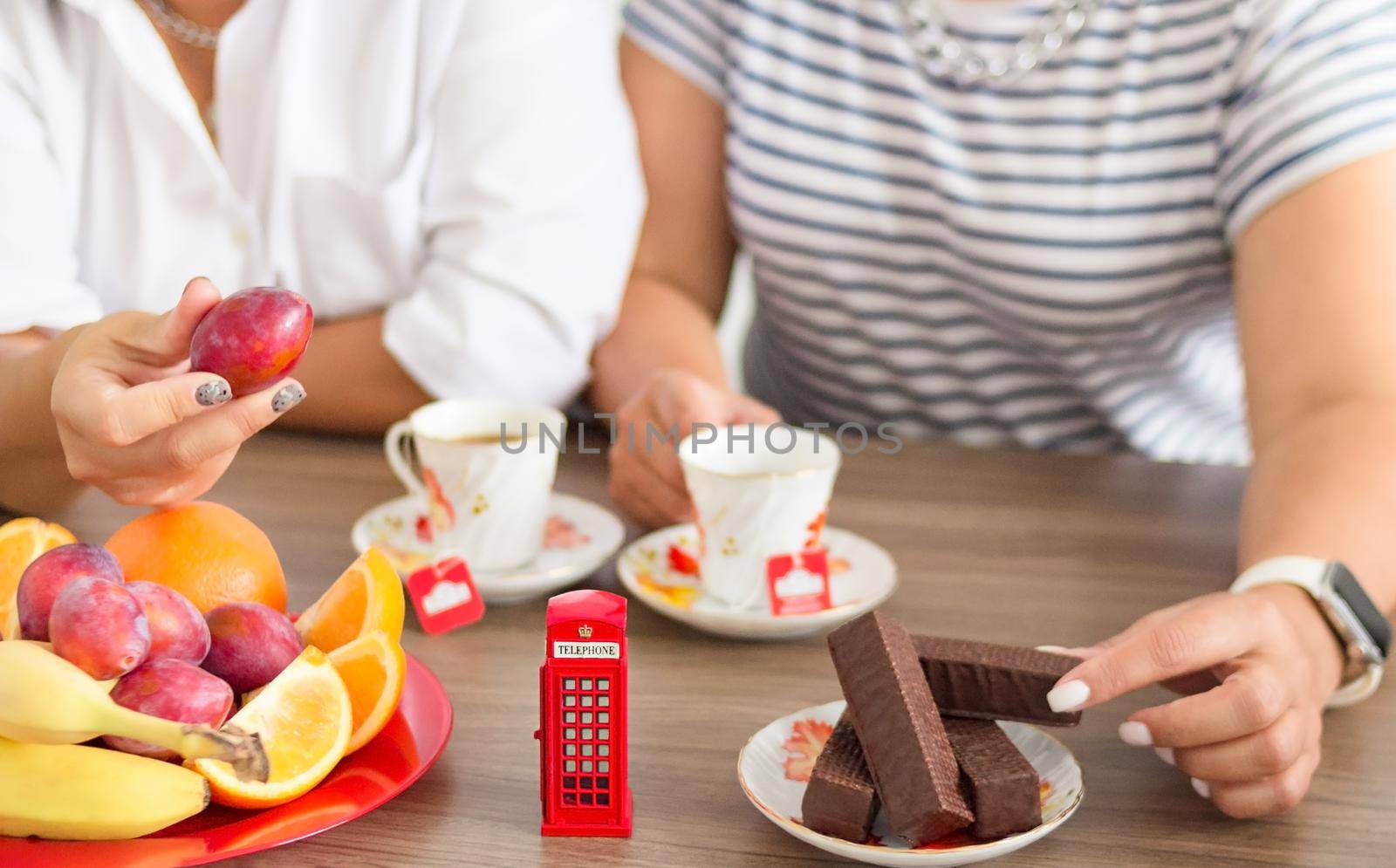 Traditional afternoon tea of british ceremony with such symbol of britishness as toy telephone box, defocused faceless women on background, front focus