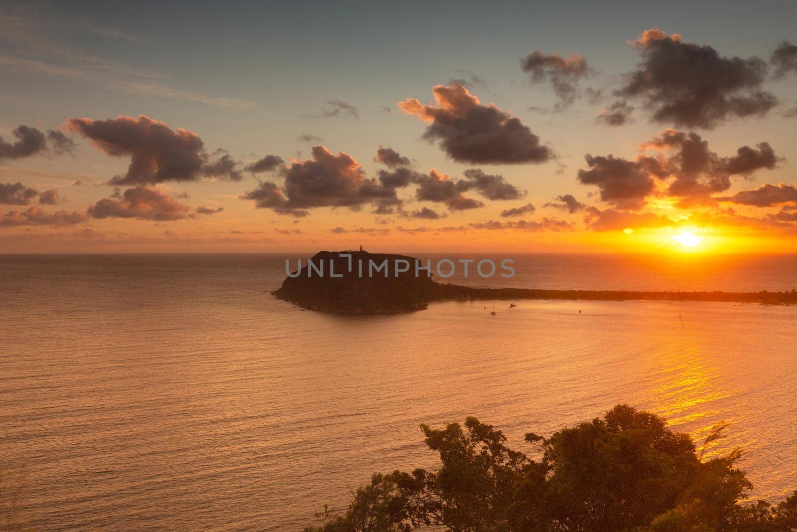 Pretty sunrise over Palm Beach and Barenjoey Lighthouse, with clouds edged in pink and a golden orange light streaming across the sea