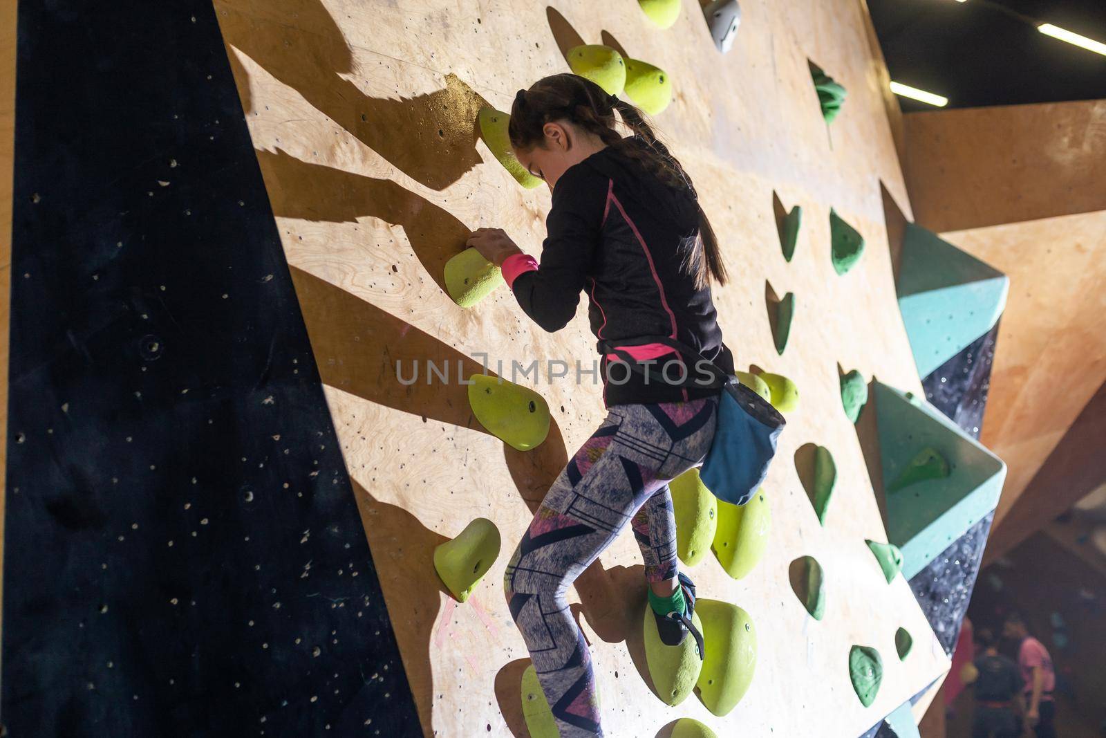 Junior Climber Girl shirt hanging on holds on climbing wall of indoor gym.
