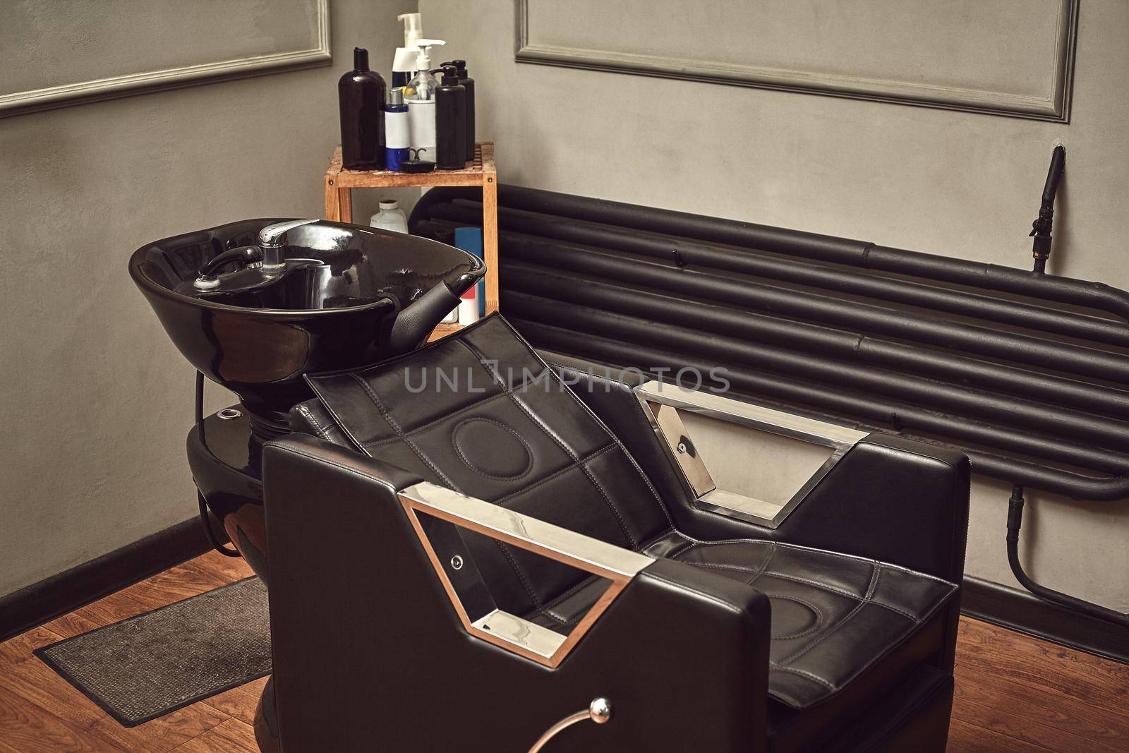 Black leather seat with wash basin in a barbershop interior with towels and shampoo on the side. by nazarovsergey