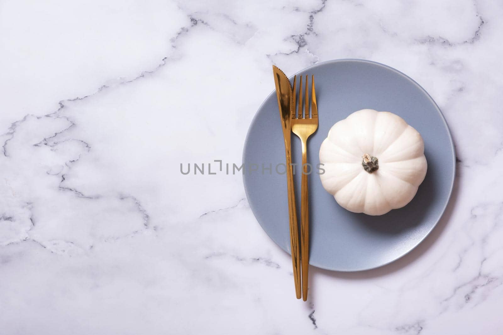 White pumpkin on a blue plate with cutlery. Minimalist concept of the autumn menu.