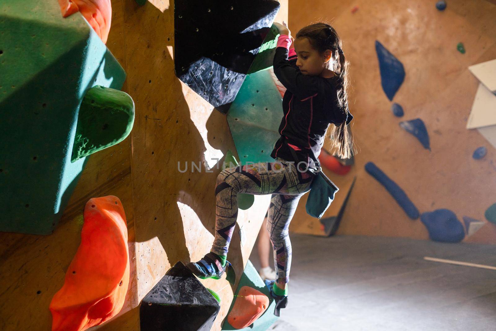 Junior Climber Girl shirt hanging on holds on climbing wall of indoor gym.