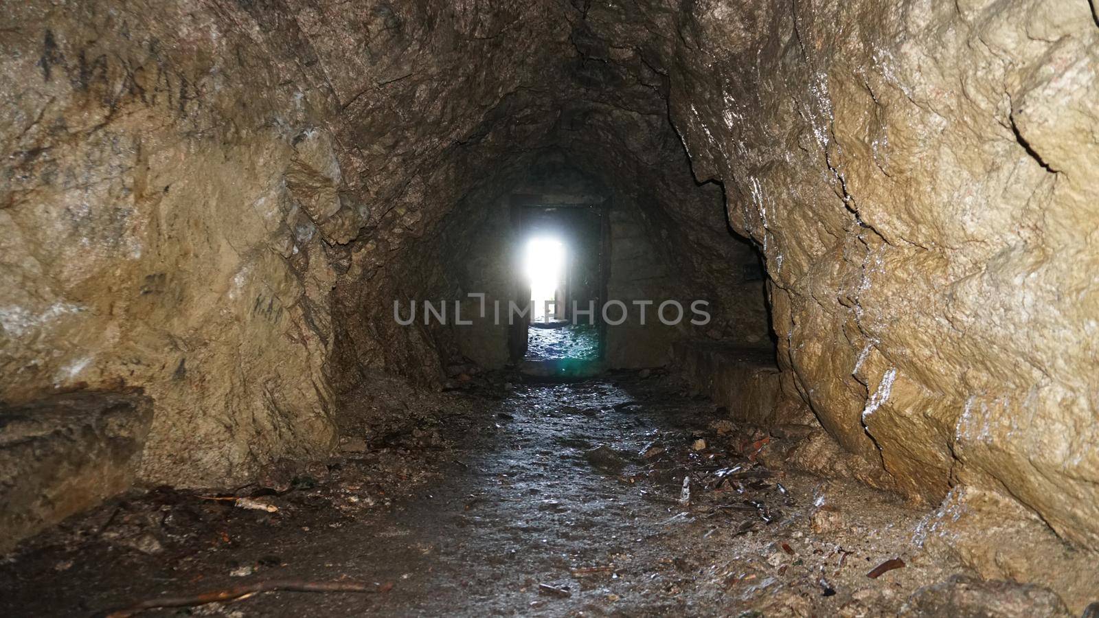 Light and exit at the end of the wet cave. The rays of the sun fall on the stone damp walls. An artificial cave in the mountain. A passage to the video door was made. Bright light at the end of tunnel