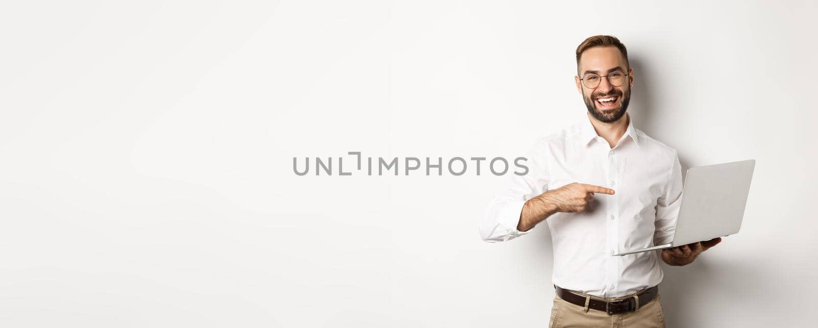 Business. Handsome manager in glasses working on laptop, pointing at computer and smiling pleased, standing over white background.