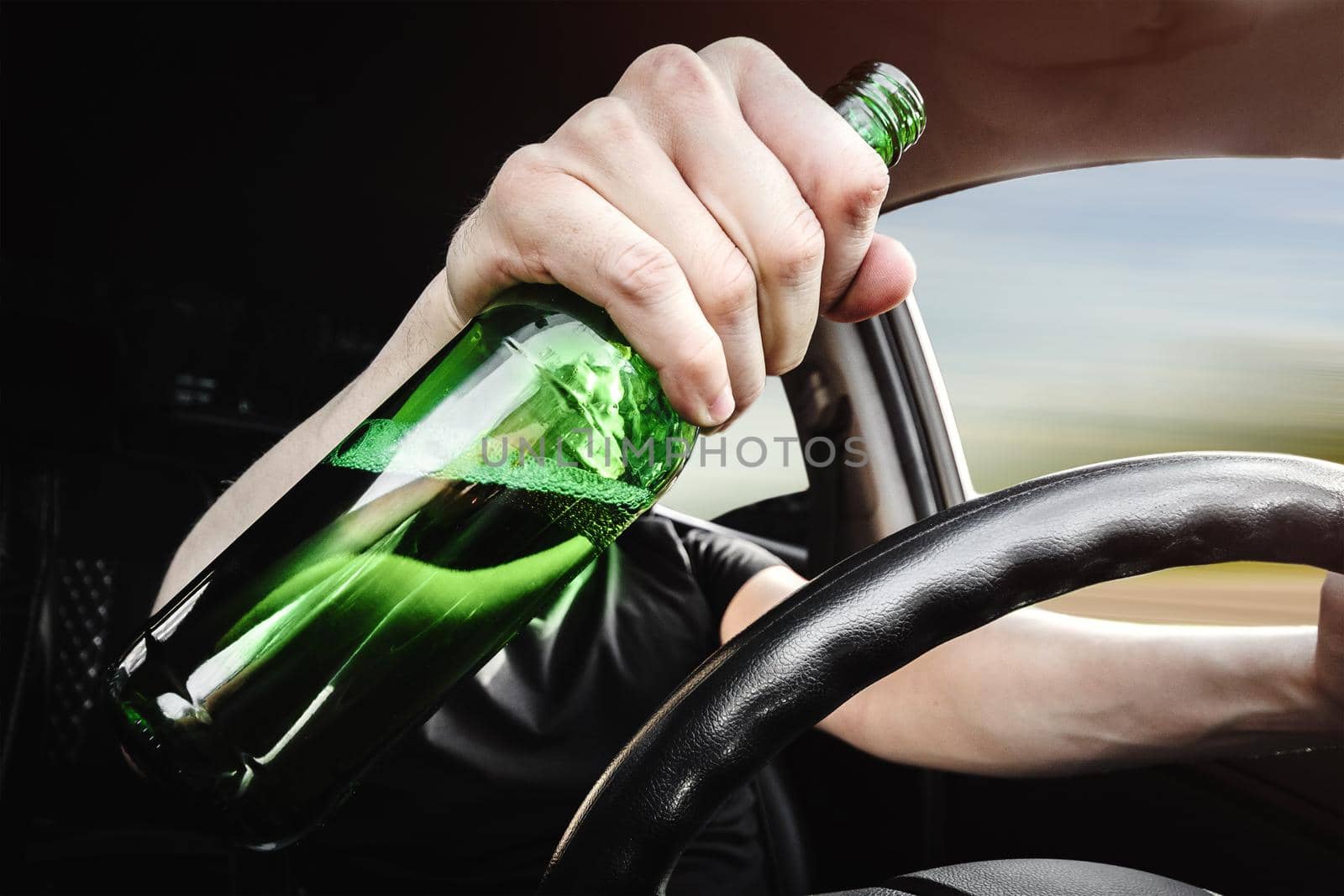 Close-up of a bottle of beer in the driver's hand at the wheel. Alcohol driving concept.