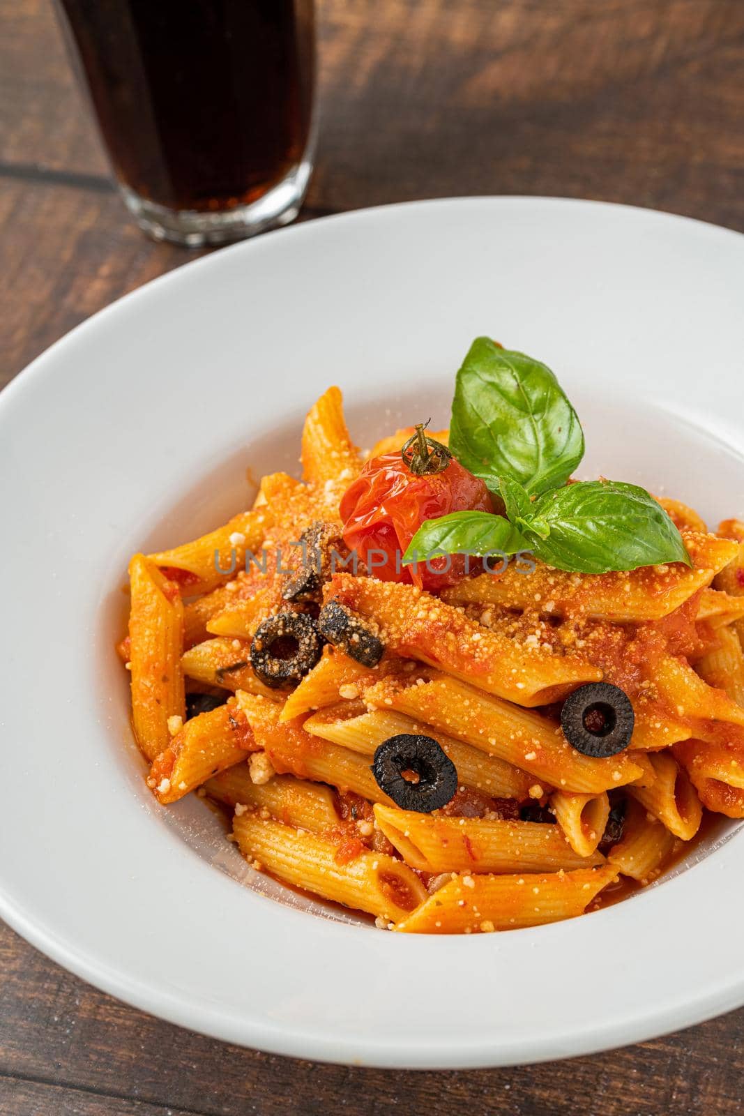 Penne pasta in tomato sauce, tomatoes decorated with parsley on a wooden background