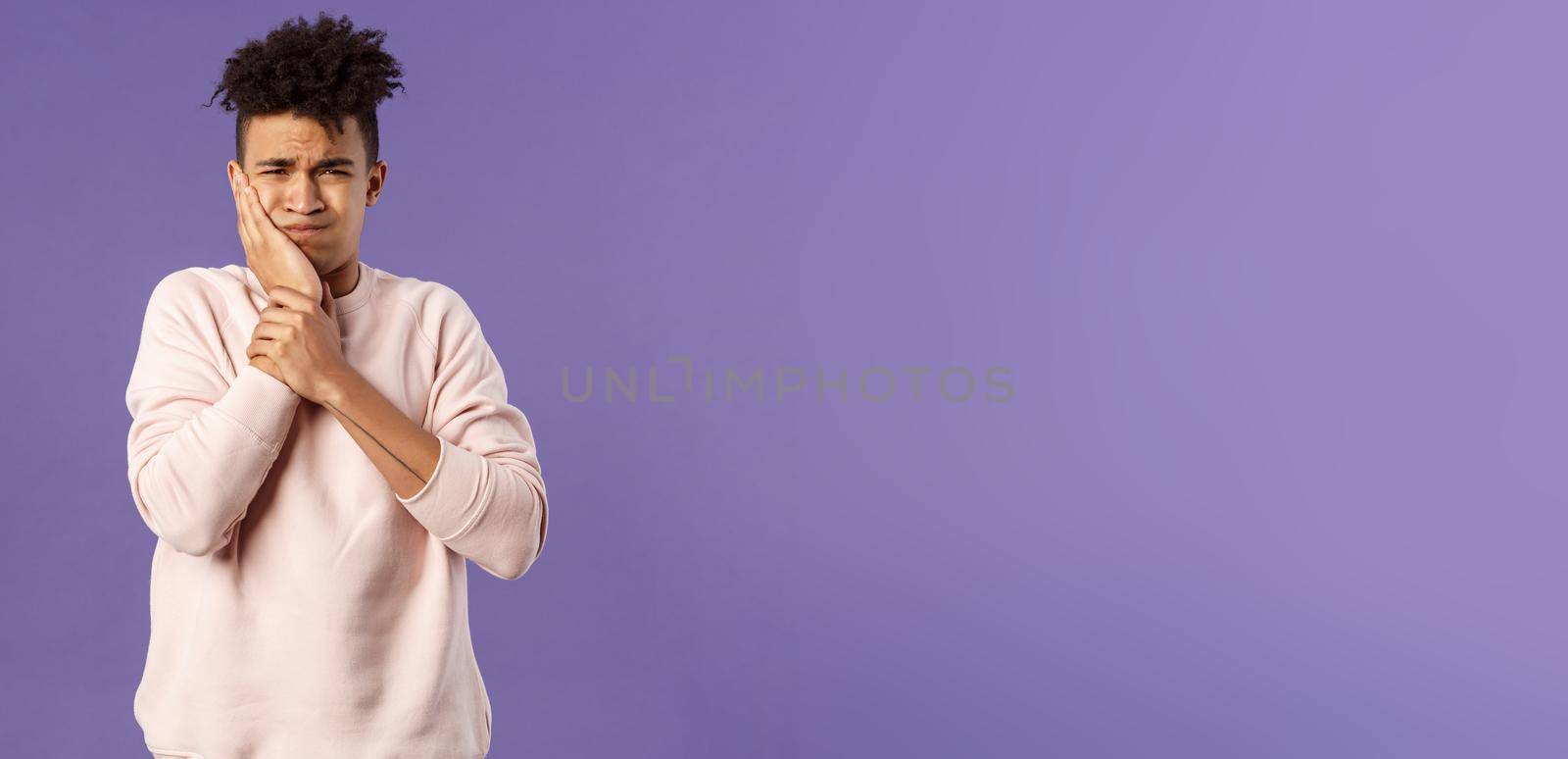 Portrait of troubled young man feeling painful ache in tooth, have toothache or decay, touching swallen cheek grimacing uneasy, need see dentist, waiting in line for appointment, purple background.