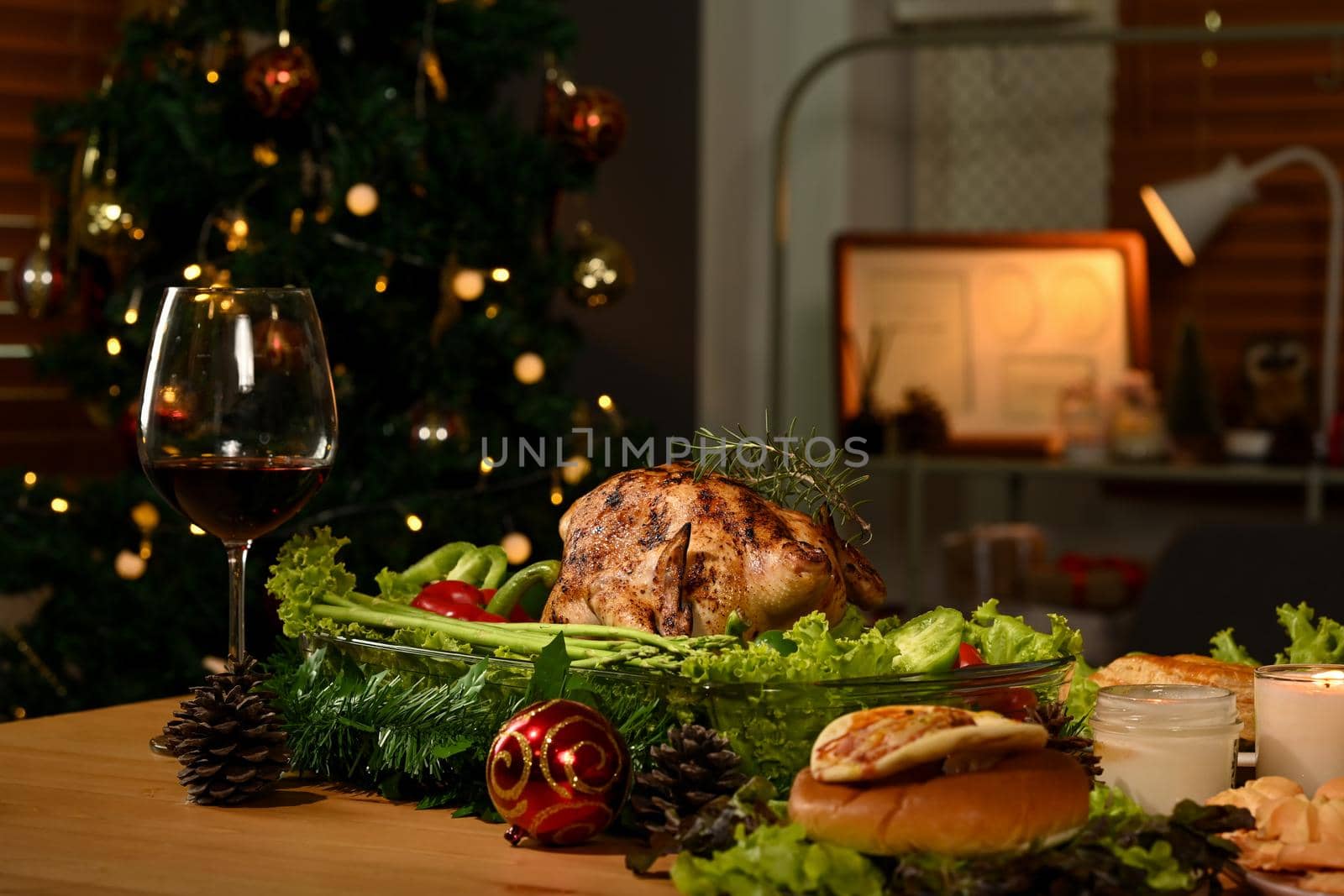 Thanksgiving table with roasted turkey, red wine and sides dishes in decorated room with a Christmas tree.