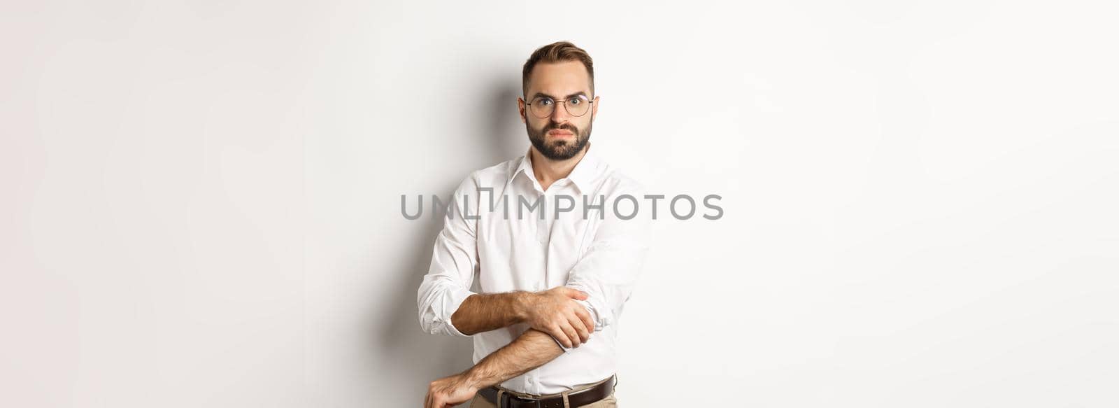 Angry man roll up sleeves and looking offended, getting ready to fight, standing over white background.