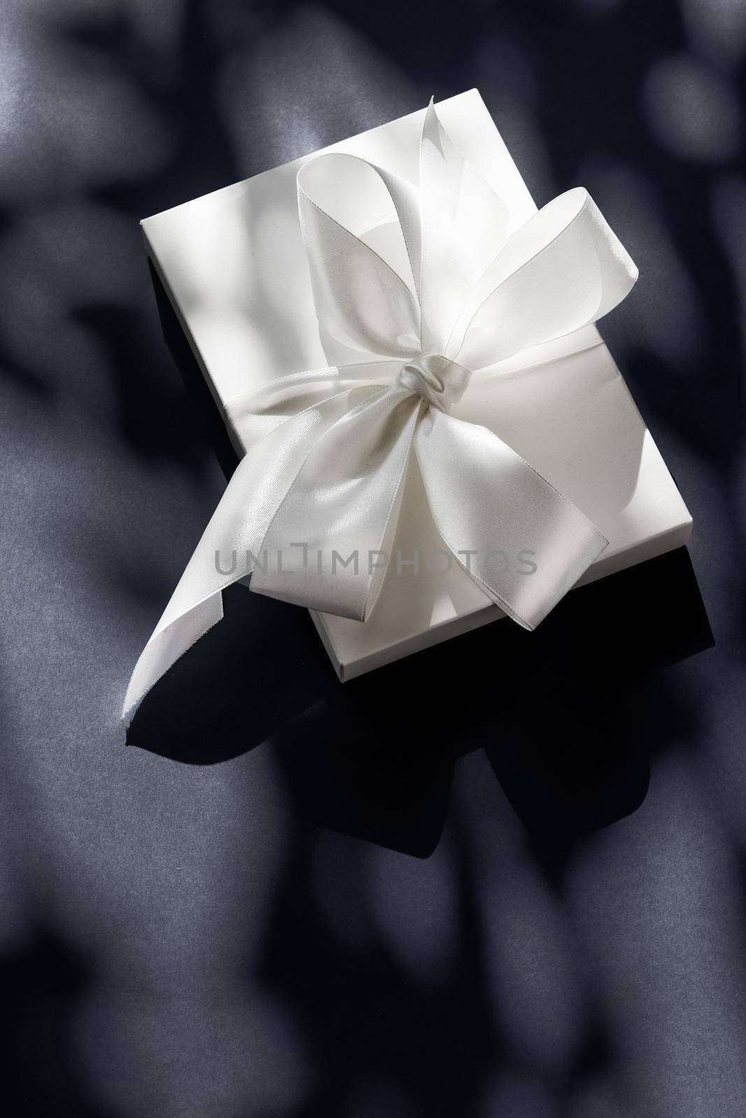 Luxury holiday white gift box with silk ribbon and bow on black background, luxe wedding or birthday present by Anneleven