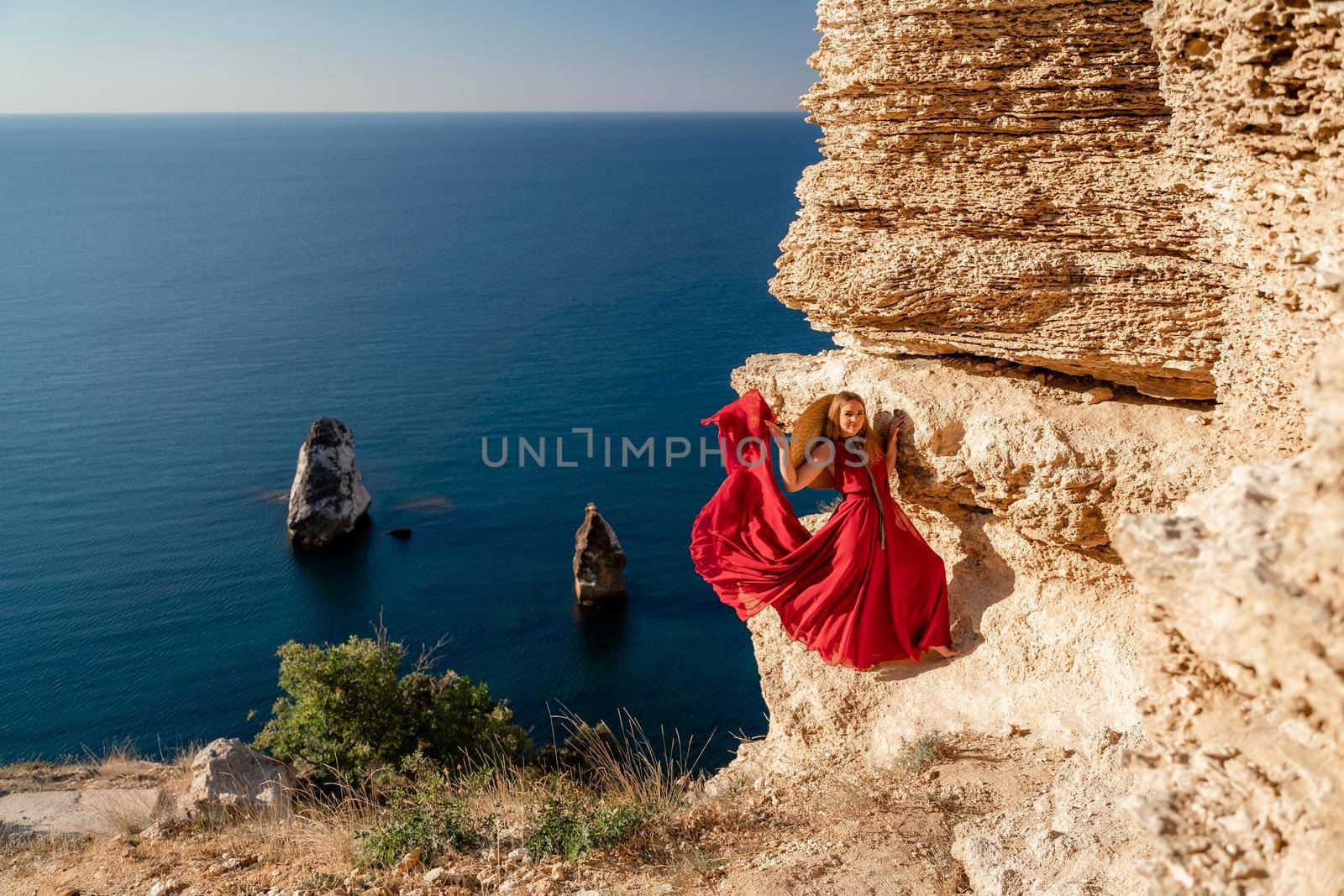 A woman in a red flying dress fluttering in the wind, against the backdrop of the sea. by Matiunina