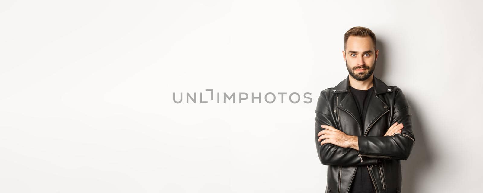Attractive macho man in leather jacket smiling, looking confident with hands crossed on chest, white background by Benzoix