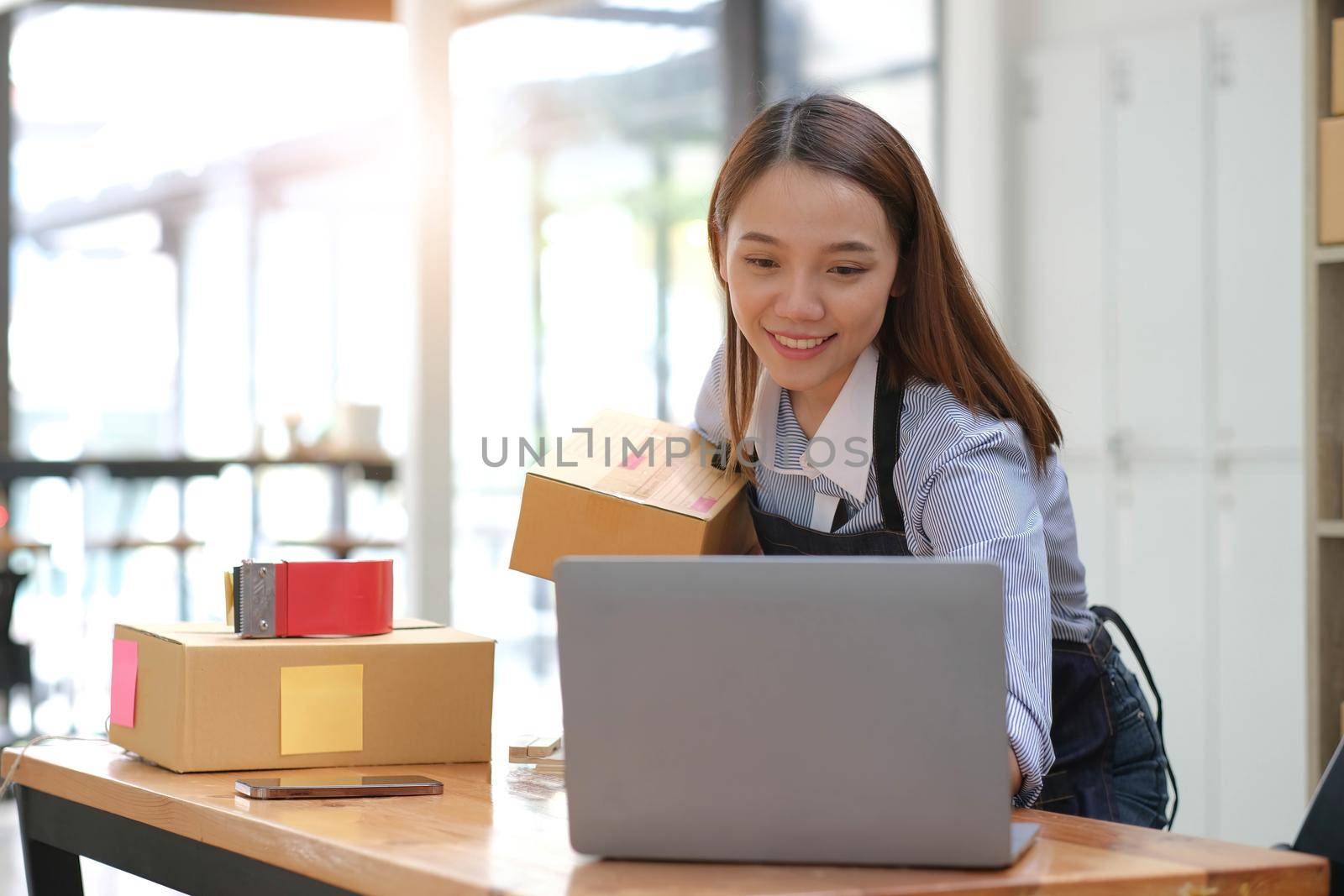 Portrait of Asian young woman SME working with a box at home the workplace.start-up small business owner, small business entrepreneur SME or freelance business online and delivery concept. by wichayada