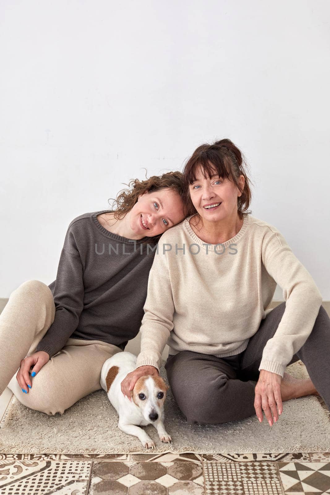 Cheerful adult daughter and middle aged mother sitting on floor with cute dog at home