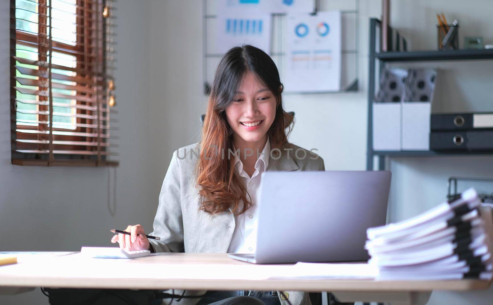 Beautiful Asian businesswoman analyzes charts using laptop calculator at the office..