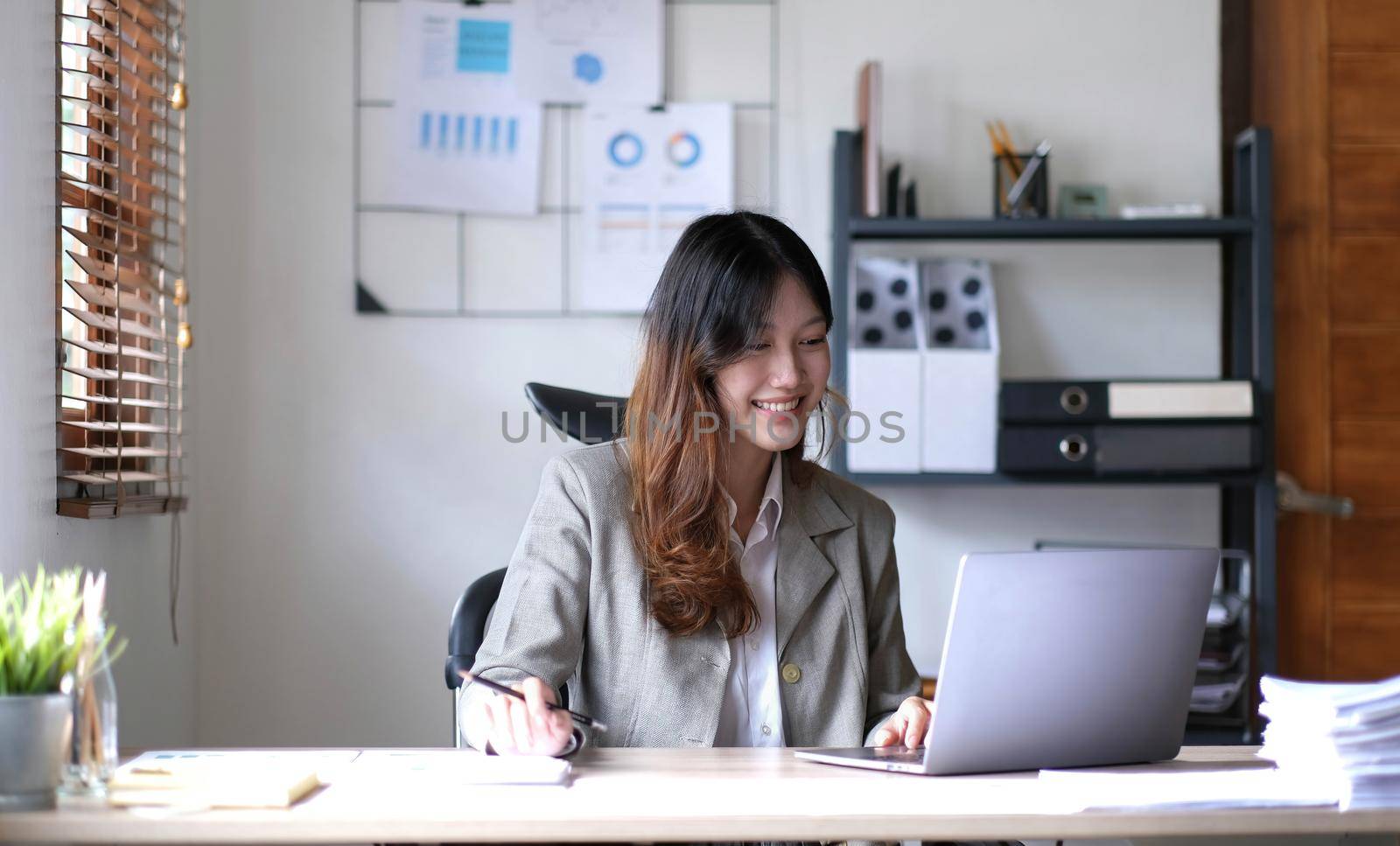 Beautiful young smiling Asian businesswoman working on laptop. Asia businesswoman working document finance and calculator in her office. by wichayada