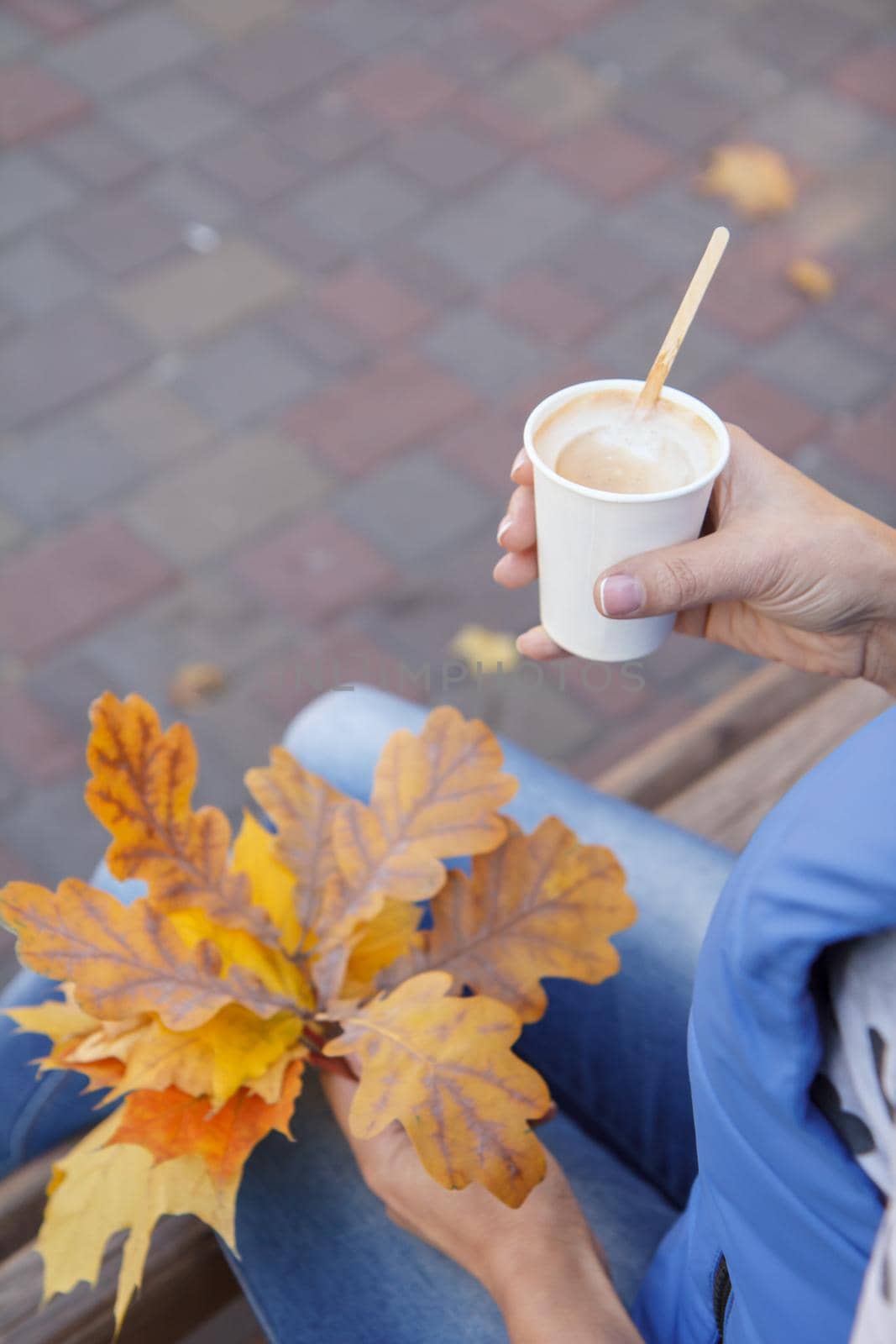 Close-up view of young woman with a cup of coffee and dry autumn leaves in her hands. Top view. Autumn composition.