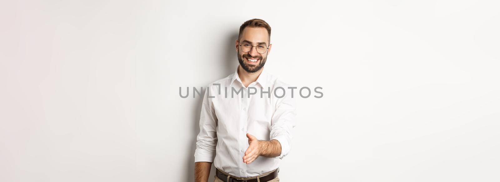 Confident businessman extending hand for handshake, greeting business partner and smiling, standing over white background.