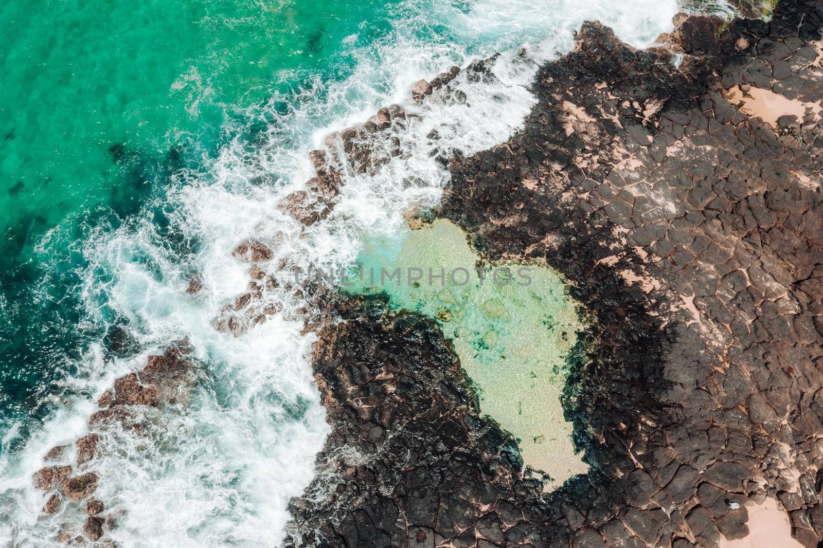 Aerial view of coastal rock pool and ocean waves flowing over the rock shelf