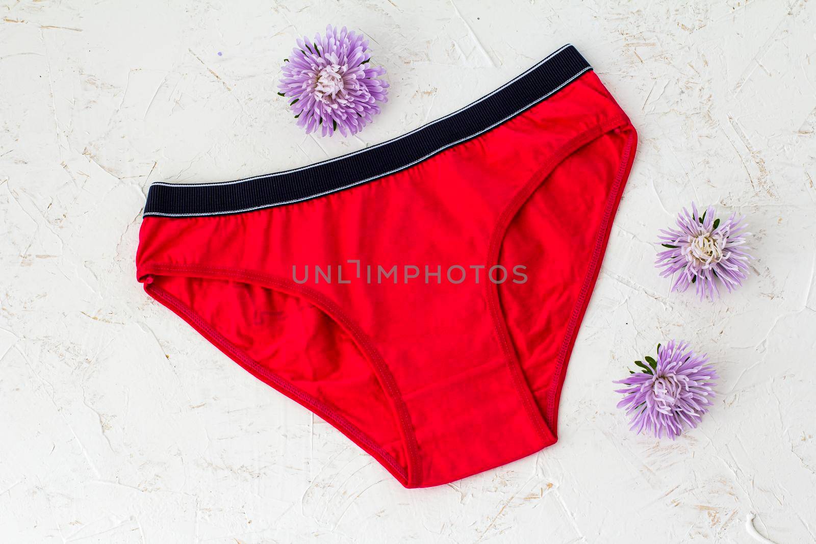 Red cotton panties with flower buds on the white structured background. Woman underwear set. Top view.