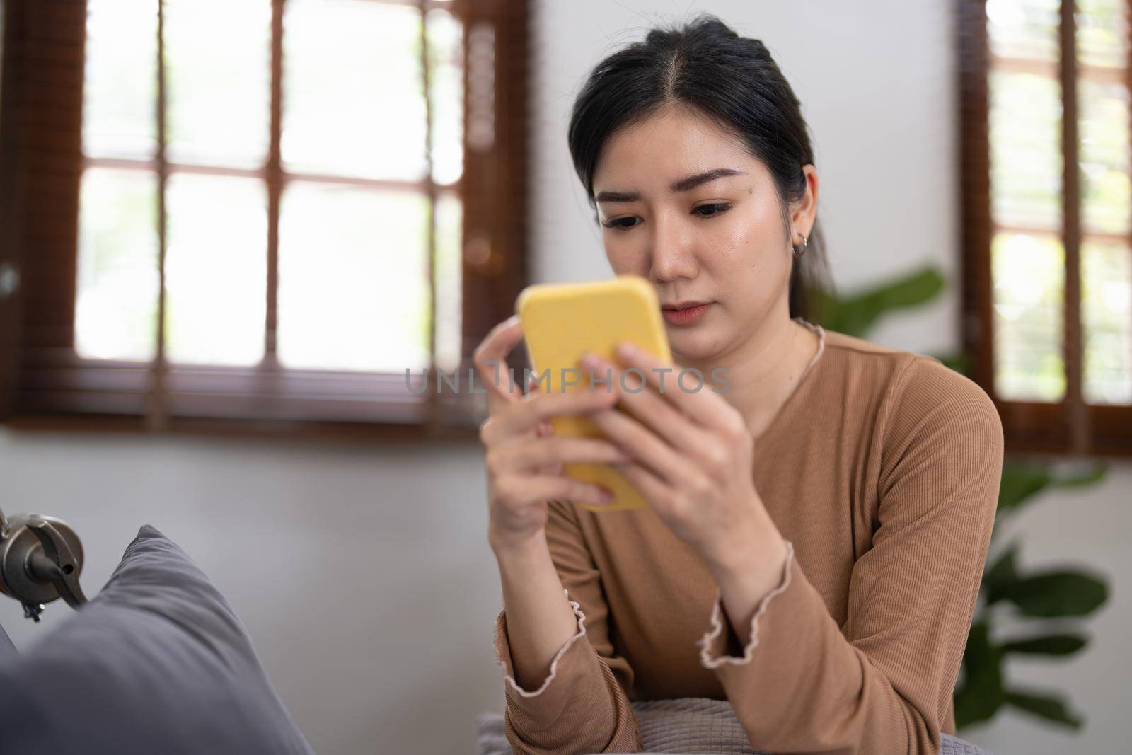 Cropped shot of asian young woman using smart phone at home, messaging or browsing social networks while relaxing on couch.